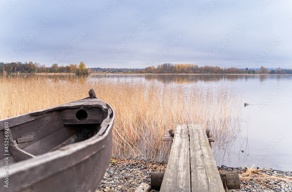 Obraz premium Old wooden boat on the shore of beautiful misty lake and autumn forest landscape. Autumn forest and lake background. Great design for any purposes.