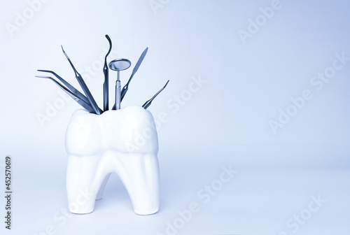 Dental professional steel tools in tooth shaped holder on blue background. Set of metal medical equipment tools for teeth dental care. sickle probe, dental explorer, mirror, burnisher, forceps