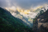 Mountains in low clouds in overcast evening in Nepal. Moody landscape with beautiful high rocks and dramatic cloudy sky, sunlight, green forest in fog at sunset. Nature background. Himalayan mountains