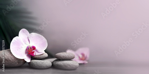 Spa stones with palm branch and flower orchid on grey background.
