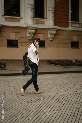 Young bearded tattooed man. A romantic guy in a white shirt, cap and suspenders walks in the city. revolves around a lamppost. Peaky Blinders. old-fashioned, retro.