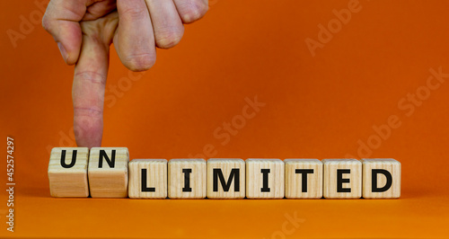 Limited or unlimited symbol. Businessman turns cubes, changes words 'limited' to 'unlimited'. Beautiful orange background, copy space. Business, limited or unlimited concept. photo
