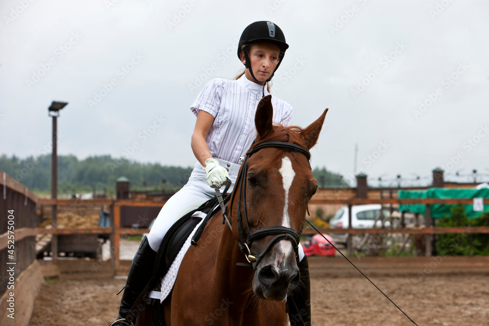 A girl in white equestrian clothes and a helmet, riding a brown horse. he performs at a competition, a very serious person.