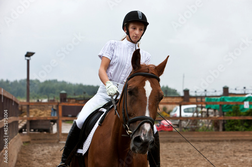 A girl in white equestrian clothes and a helmet, riding a brown horse. he performs at a competition, a very serious person.