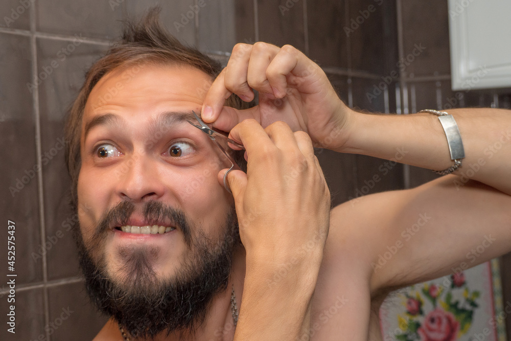 Obraz premium A bearded man cuts his eyebrows