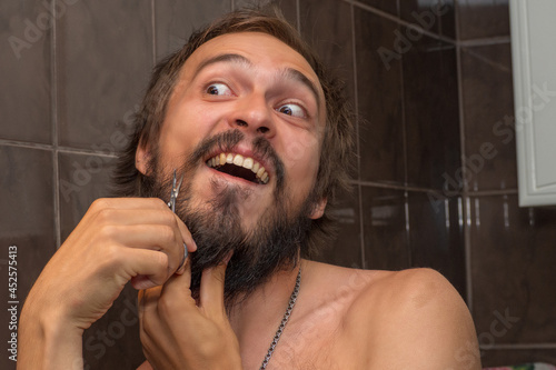 Bilde på lerret A bearded man trims his beard with small scissors