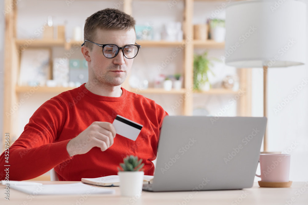 a European man in a red jumper makes a purchase online, orders food or delivers purchases, modern technologies, order a delivery service, contactless delivery and payment for food and clothing on the