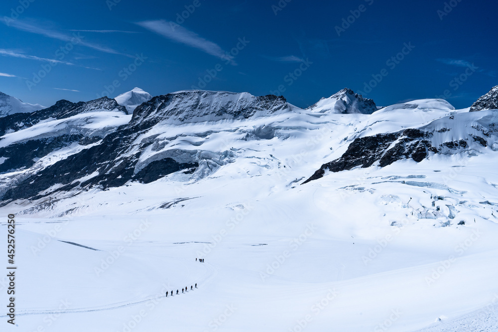 une file de randonneurs au milieu de hautes montagnes enneigées