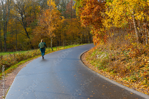 Person walking by the side of a road by a forest at fall.