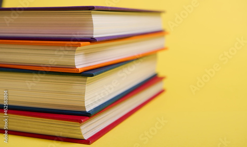 Close-up of stacked multicolored books on yellow surface background with copy space for text. Teacher s Day concept  Knowledge  literature  reading  erudition