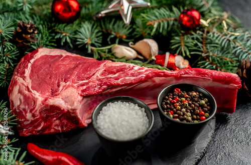 Christmas raw tomahawk steak with Christmas tree decorations on stone background