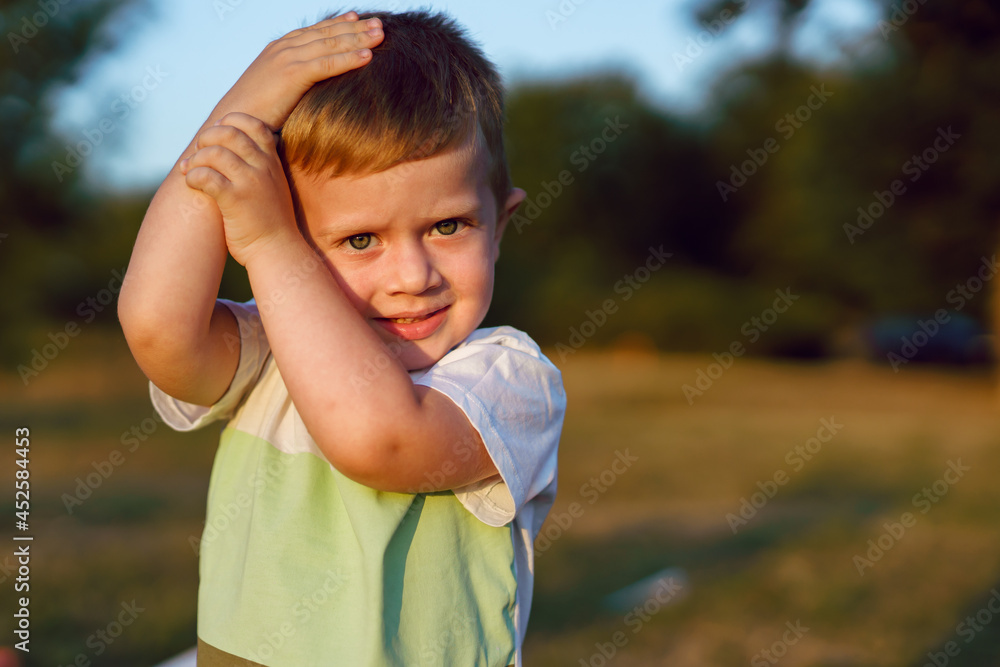 Portrait of small caucasian boy three years old looking to camera in sunny summer or autumn evening warm tone copy space blonde caucasian kid hold hands on head to defend from violence in the field Portrait of small caucasian boy three years old looking to camera in sunny summer or autumn evening warm tone copy space blonde caucasian kid hold hands on head to defend from violence in the field