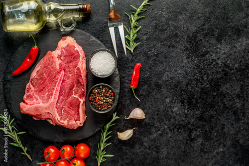 raw T-bone steak with spices ingredients on a stone background with copy space for your text