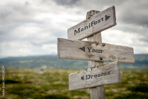 manifest your dreams text quote on wooden signpost outdoors in nature. photo