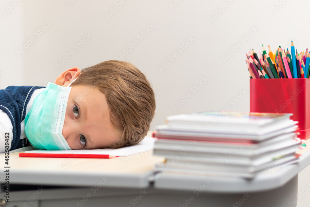 A cute first grader boy in a school uniform at his desk wearing a protective medical mask during the coronavirus pandemic. Selective focus. Close-up. Portrait A cute first grader boy in a school uniform at his desk wearing a protective medical mask during the coronavirus pandemic. Selective focus. Close-up. Portrait
