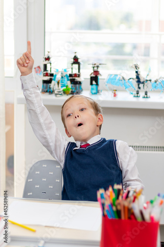 Cute boy first grader in school uniform at home during a break fooling around while sitting at his desk. Selective focus. Close-up. Portrait