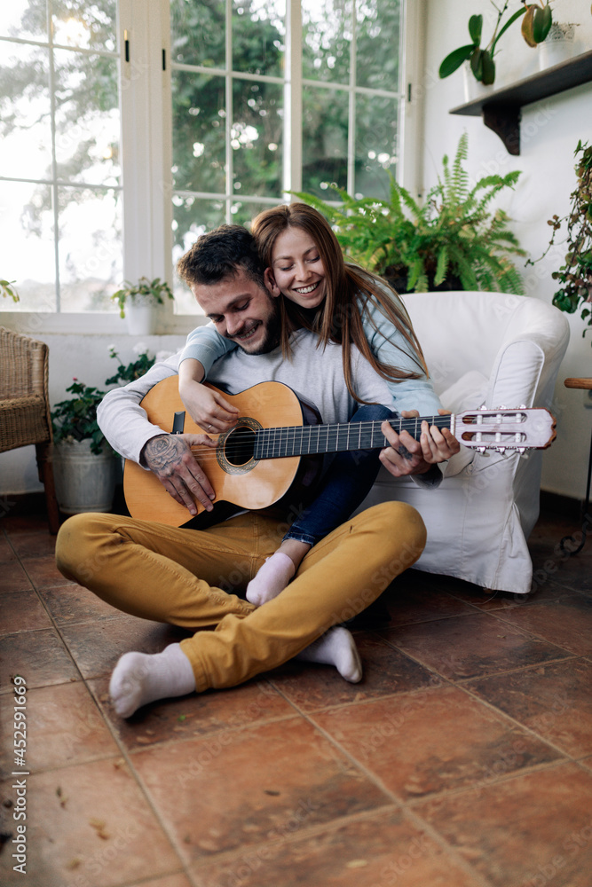 Smiling guitarist playing guitar while interacting with girlfriend at home Smiling guitarist playing guitar while interacting with girlfriend at home