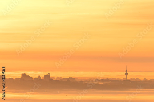 Modern cityscape with skyscrapers and tower building with clouds and ground fog partially covering the buildings in orange sunrise. Madrid, Spain