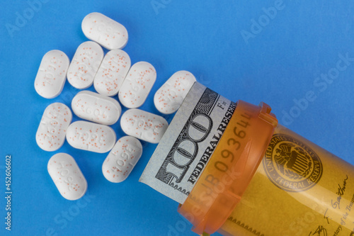 Hydrocodone tablets with a hundred dollar bill and a pill bottle. Opiate addiction costs the U.S. economy $78.5 billion per year. photo