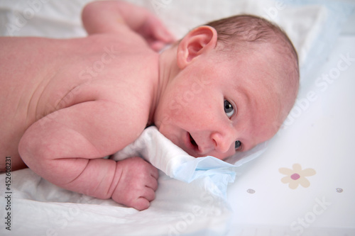 A baby aged one month is lying in a crib on his stomach. A Caucasian boy child in a home white bedroom