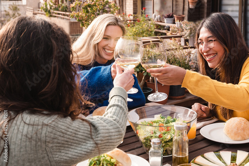 Multiracial friends eating vegan food cheering with wine outdoors at patio restaurant - Focus on center girl eye