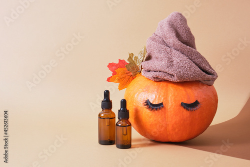 mock up cosmetic containers with pipettes and pumpkin with towel and eyelashes on beige background, skin care in autumn