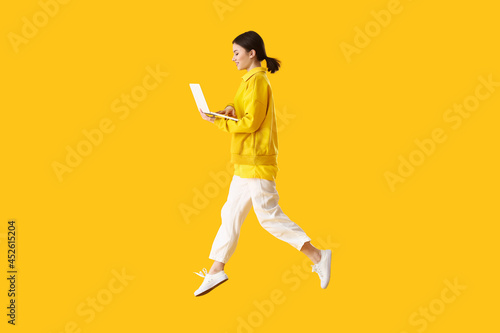 Jumping young woman with laptop on color background © Pixel-Shot