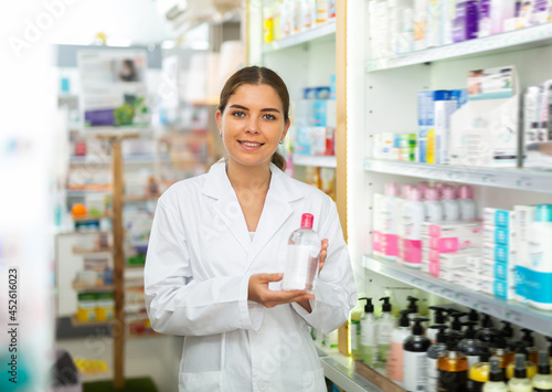 Female pharmacist in gown demonstrating skin care product in salesroom of drugstore