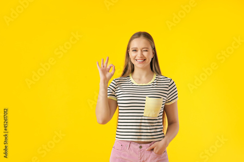 Young woman showing OK on color background