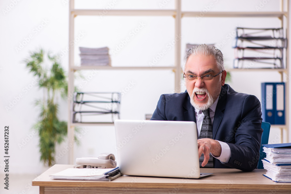 Old male employee unhappy with excessive work in the office Old male employee unhappy with excessive work in the office