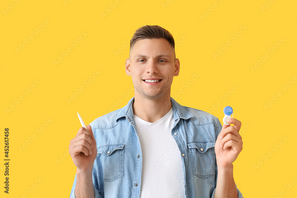Young man with contact lenses and tweezers on color background