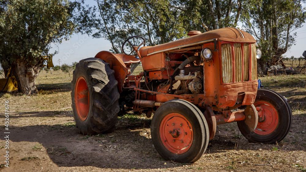 old rundown orange tractor parked outdoors. old rundown orange tractor parked outdoors.