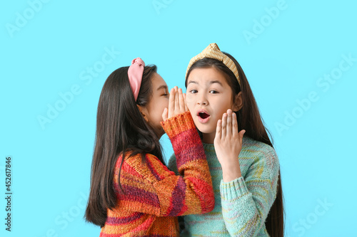 Cute little girls telling secrets to each other on color background photo