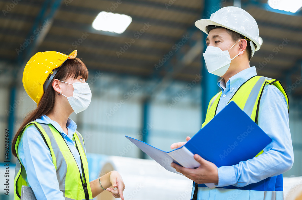 Team engineers and foreman or technicians males and females wear a mask, hard hat and vest. Standing, consult discuss industrial production management through data files within the factory. Team engineers and foreman or technicians males and females wear a mask, hard hat and vest. Standing, consult discuss industrial production management through data files within the factory.
