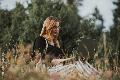 happy woman freelancer with glasses working on laptop, remote location in nature