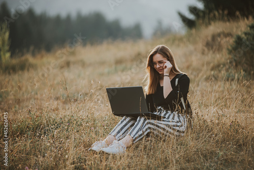 happy woman freelancer with glasses working on laptop, remote location in nature