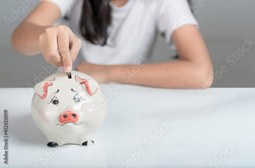 Tableau sur toile girl wearing a white shirt  hand holding a coin to drop the piggy bank