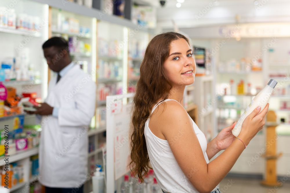 Teenager girl choosing haircare products in drugstore and pharmacist helping her with it