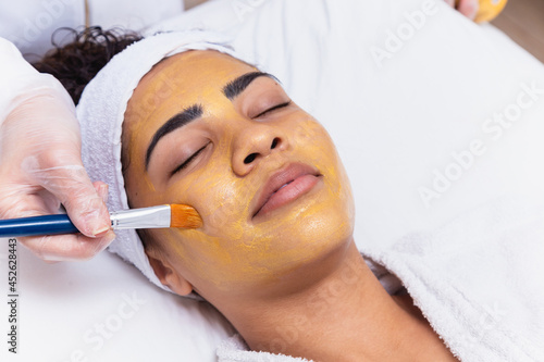 woman is lying in the cosmetologist s office on the procedure of moisturizing her face. The cosmetologist applies a moisturizing mask to the patient's face. photo