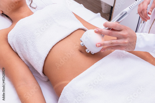 Cropped shot of a professional dermatologist performing radiofrequency lifting procedure on the stomach of a woman. Female client getting rf-lifting treatment on her belly at cosmetology clinic.