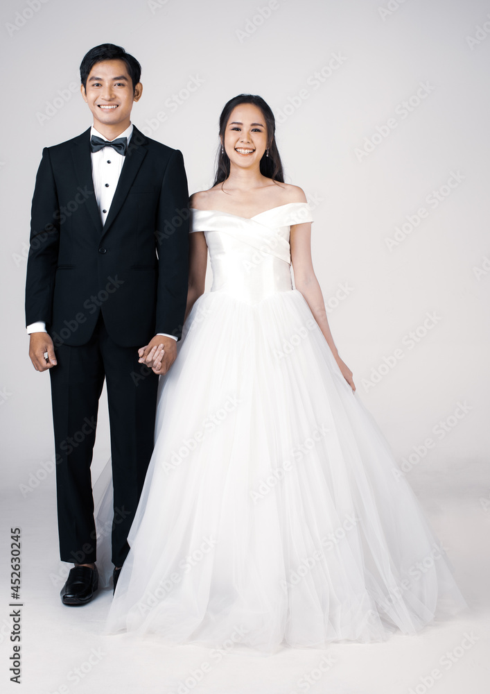 Full Length of young attractive Asian couple, soon to be bride and groom, woman wearing white wedding gown. Man wearing black tuxedo, standing together. Concept for pre wedding photography