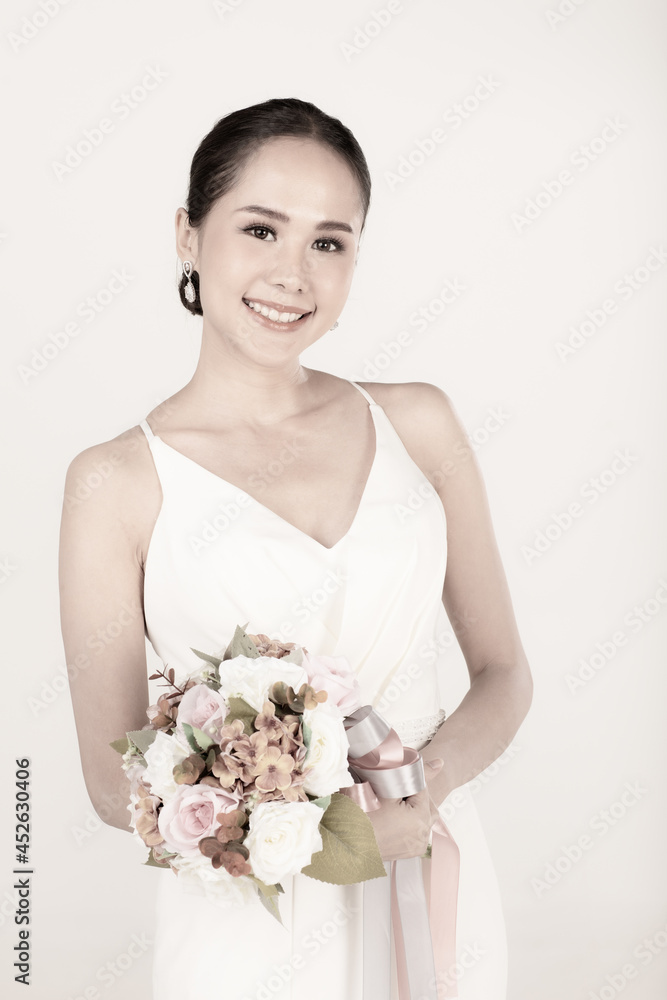 Portrait of young attractive Asian woman wearing white wedding dress smiling holding bouquet of flower in sepia. Concept for pre wedding photography