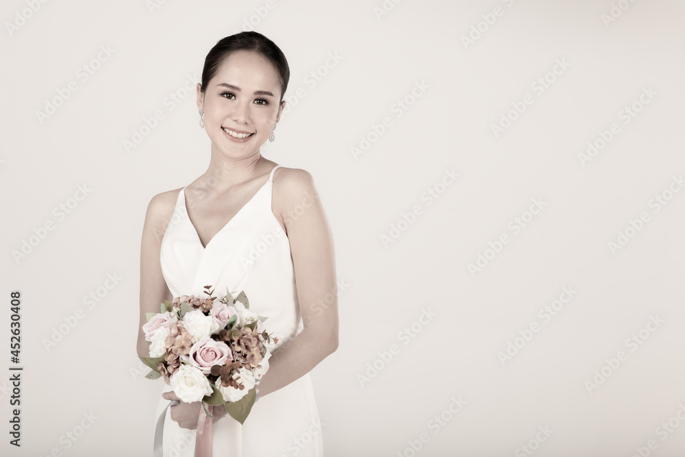Portrait of young attractive Asian woman wearing white wedding dress smiling holding bouquet of flower in sepia. Concept for pre wedding photography Portrait of young attractive Asian woman wearing white wedding dress smiling holding bouquet of flower in sepia. Concept for pre wedding photography