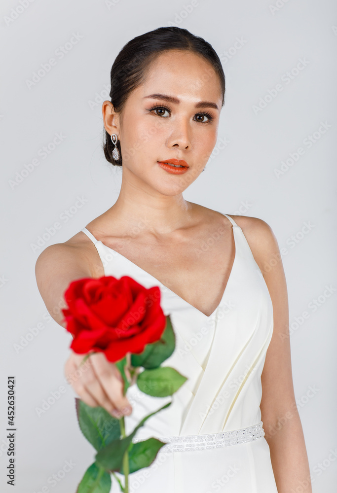 Portrait of young attractive Asian woman wearing white wedding dress holding red rose against white background. Concept for pre wedding photography Portrait of young attractive Asian woman wearing white wedding dress holding red rose against white background. Concept for pre wedding photography