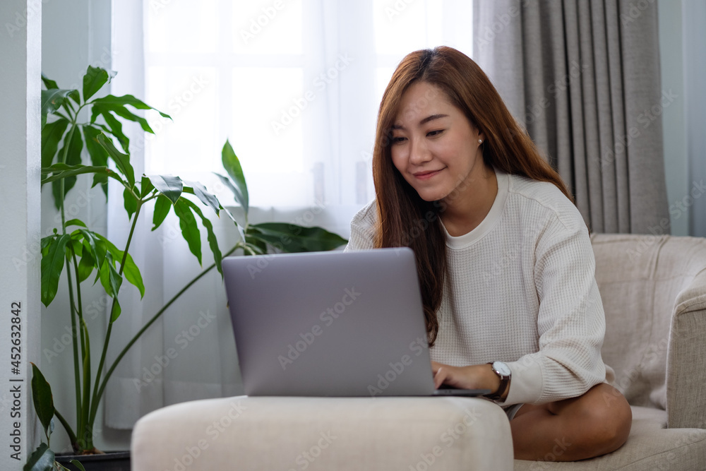 A beautiful young asian woman using and working on laptop computer while sitting on a sofa at home A beautiful young asian woman using and working on laptop computer while sitting on a sofa at home
