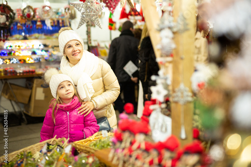 Smiling female and her daughter are choosing decorations for Christmas tree in the market outdoor. High quality photo