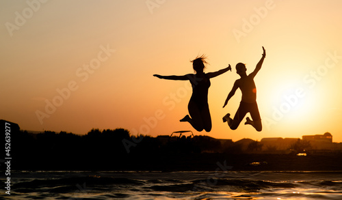 Happy friends are having fun and jump at sunset beach in sunlight. Empty space for text