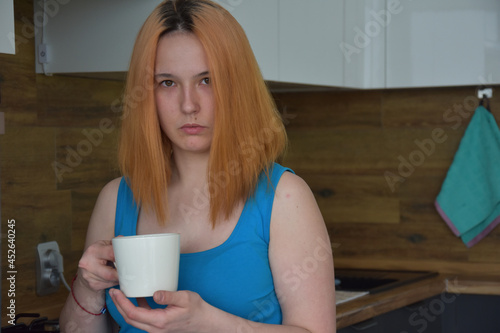 Pensive young woman drinking coffee in kitchen