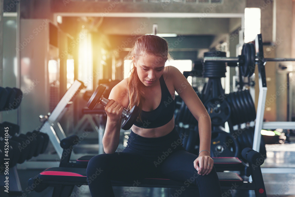 Woman lifting dumbbell weight while sitting at the gym, sports training with weight, Exercise fitness and healthy lifestyle - obrazy, fototapety, plakaty 