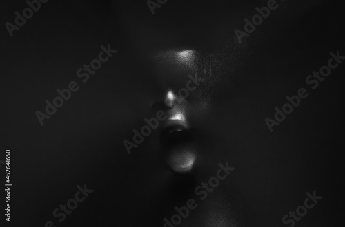 Screaming human face pressing through black fabric with shine and dark side for Halloween background concept.